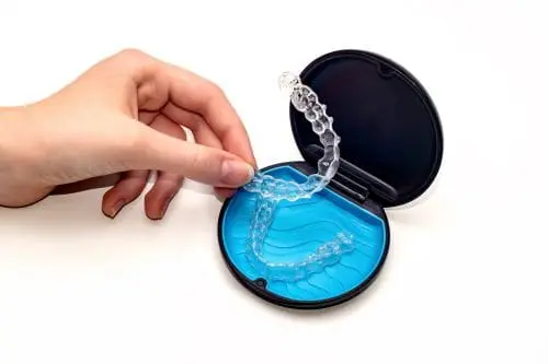 A hand removing a clear dental aligner from its protective carry case
